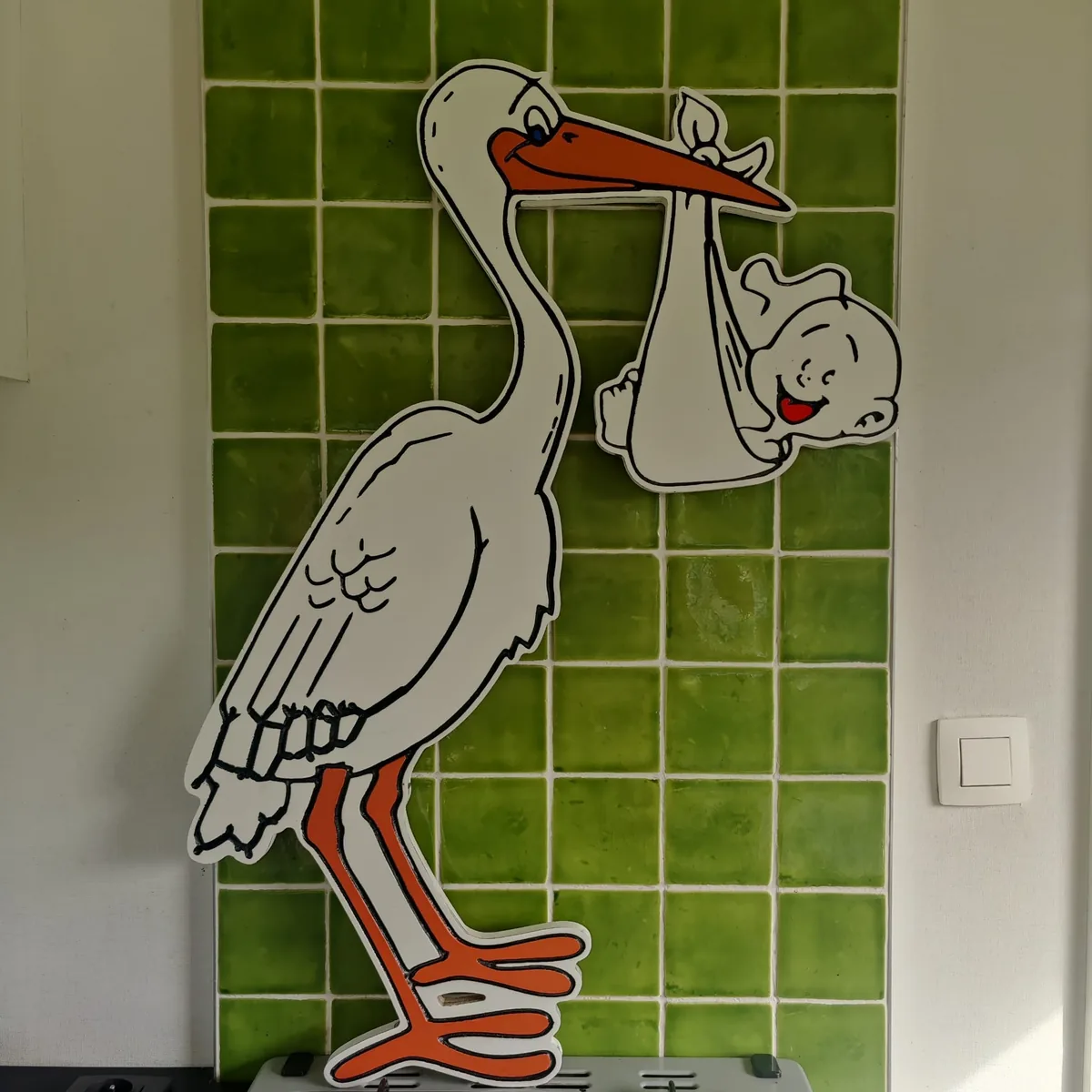 Uitgesneden en beschilderd geboortebord in de vorm van een ooievaar met baby